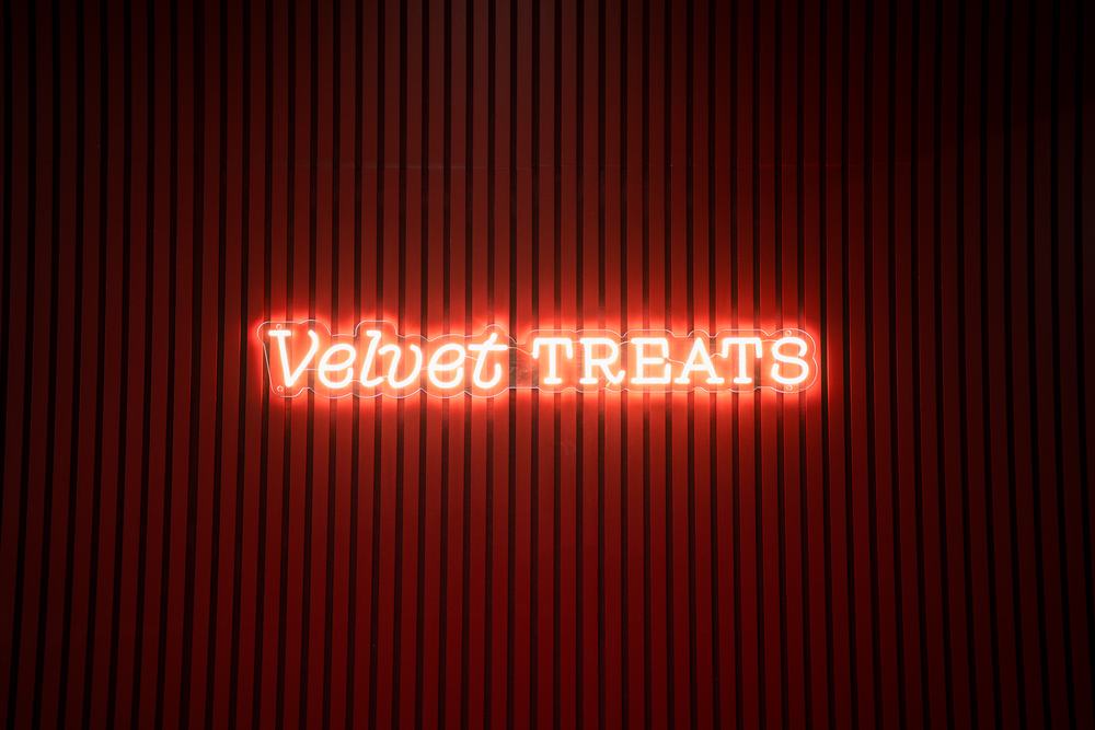 The Velvet Treats neon sign glowing on the red slat feature wall