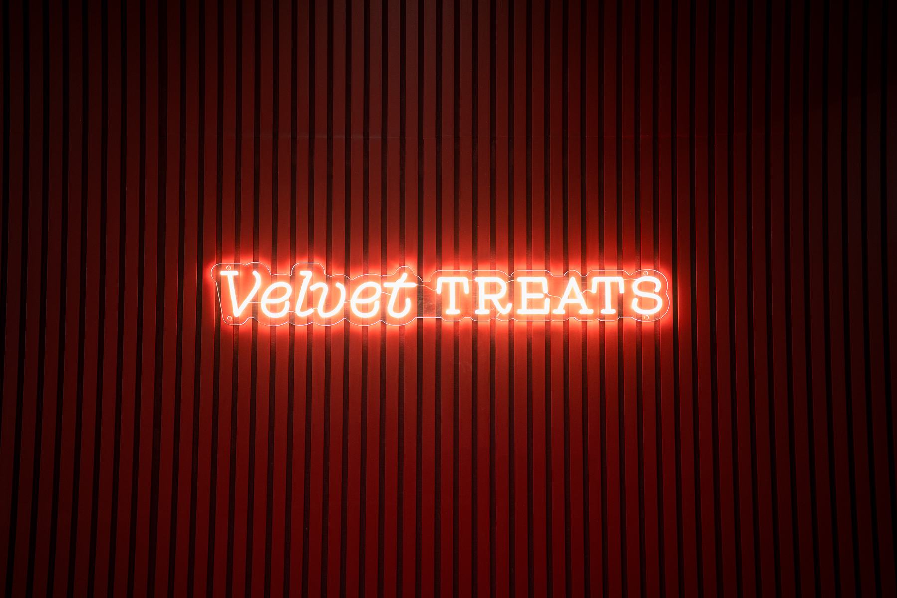 The glowing Velvet Treats neon sign on the red slat wall